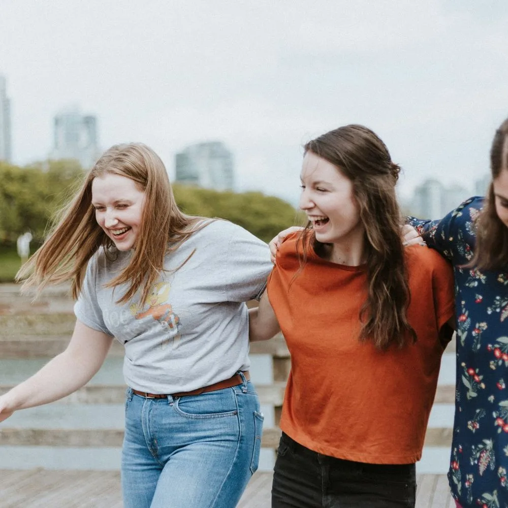 Three friends walking arm in arm outdoors, all laughing